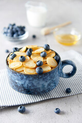 Blue Bowl of mini pancake cereal with blueberries, maple syrup and milk on concrete background. Tiny pancakes, new food trend concept. Cute healthy breakfast or snack. Recipe, menu.