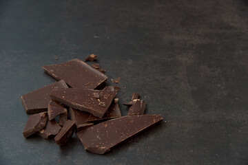 Dark chocolate stack, chips and cocoa powder on a dark background. Confectionery and food concept. Top view, copy space, selective focus..