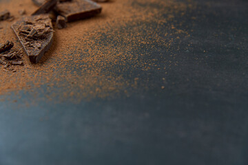 Dark chocolate stack, chips and cocoa powder on a dark background. Confectionery and food concept. Top view, copy space, selective focus..