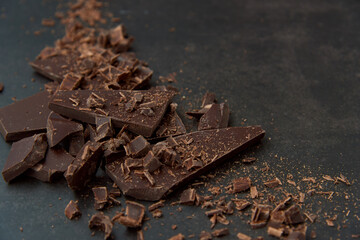 Dark chocolate stack, chips and cocoa powder on a dark background. Confectionery and food concept. Top view, copy space, selective focus..