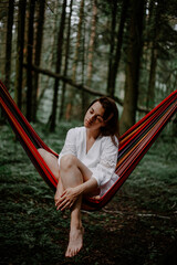 A young girl is sitting in a hammock hanging in the woods