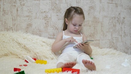 The child plays in the smartphone in the room. Distance learning of preschoolers online