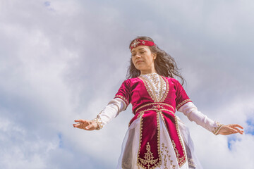 A young girl in an Armenian female national costume dances a bewitching dance against a dark cloud