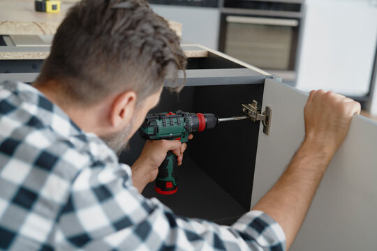 Man installing hinges in kitchen furniture