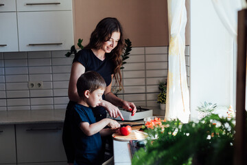 Little son helps mom cook vegetable salad cuts vegetables in kitchen