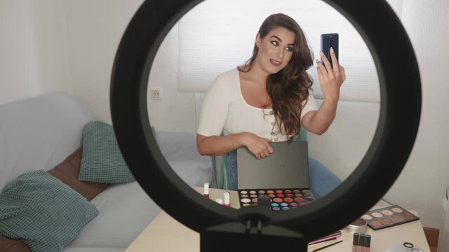 Fashion blogger presenting make-up cosmetics at home by filming himself with his mobile phone. Influencer in the concept of social media.