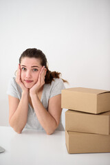 Vertical portrait of a cute girl supports her head with her hands leaning on a table. Cardboard boxes on a table on a light background