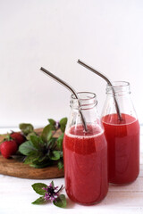 Red smoothies from fresh strawberries and basil in glass bottles with reusable stainless steel straws. Zero waste concept.