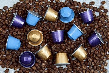 Obraz na płótnie Canvas Caffeine, hot drinks and objects concept. Close up colorful capsules or pods for coffee mashine with some roasted grains on gray concrete background. Top view with space for text. Selective Focus.
