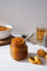 Apricot jam in a glass jar on a white wooden surface. Homemade preservation concept. Selective focus.
