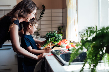 Little son helps mom cook vegetable salad in the kitchen