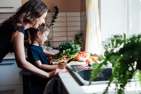 Little son helps mom cook vegetable salad in the kitchen