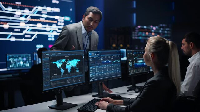 Confident Female Specialist Works on Computer Talks with Team Leader in Big Infrastructure Control Room. Business Woman Professional Uses Computer Showing Charts, Information. Monitoring Room Teamwork