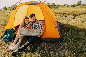 Couple of young man and woman sitting in an orange tent in mountains, looking to a map. © Bostan Natalia