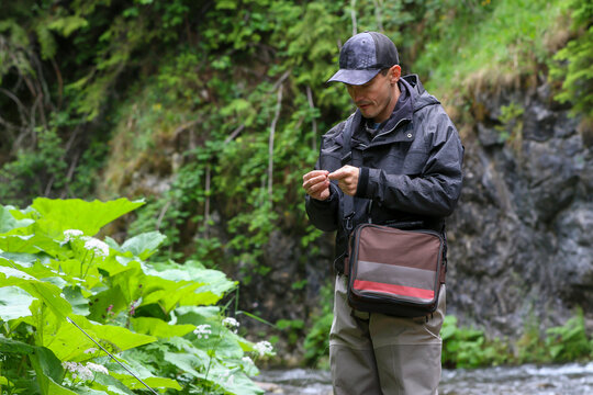 Shot of a fishing man tying a bait to his fishing rod. Close up of hands of a person fixing a bait to a fishing rod to catch fish.
