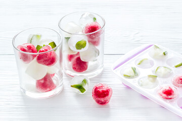Cocktail glasses with berries in ice cubes on white table