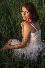 Portrait of a beautiful girl having fun among the red flowers on the poppy field. Young woman smiling and holding a flower in her hands on the sunset. Soft selective focus.