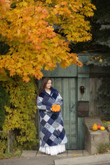 Russian girl in patchwork coat with mini decorative pumpkins. Autumn, fall day, yellow leaves of maple tree. Russian village, rural house, halloween decor in Russia. Autumn nature, scenery, fall view