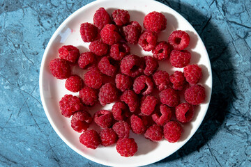 a lot of sweet fresh red raspberries on a plate from the market or garden