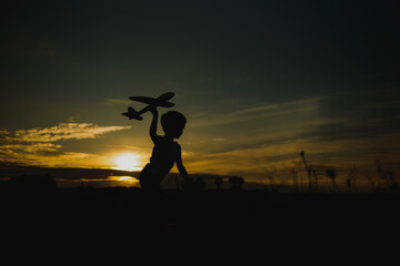 Naklejka na ściany i meble Kid boy playing with toy plane during sunset time. Childhood memories - beautiful sky over meadow. Childhood dream imagination concept