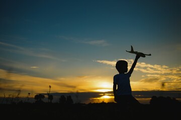 Kid boy playing with toy plane during sunset time. Childhood memories - beautiful sky over meadow. Childhood dream imagination concept