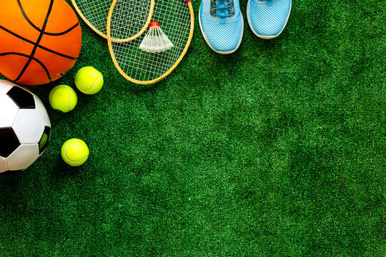 Sport games equipment - balls, sneakers, rockets - on grass top view copy space