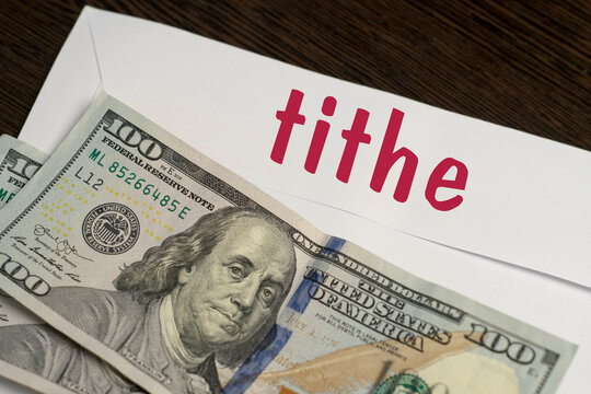 White envelope with the inscription tithe and dollar bills lie on a wooden table. Manage your finances and save money concept. Close-up