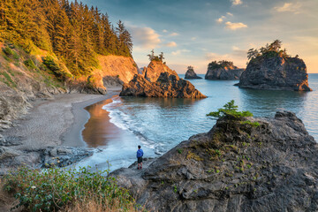 sunset over Samuel Boardman state scenic corridor on the Oregon coast with a hiker standing on the...
