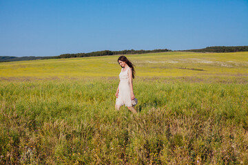 Fototapeta na wymiar Beautiful woman in dress walks on the field with yellow flowers