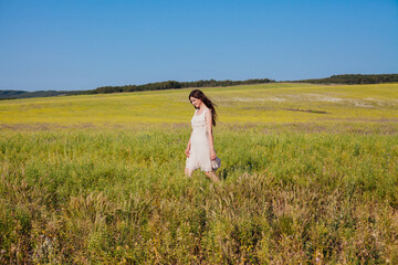 Beautiful woman in dress walks on the field with yellow flowers