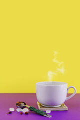 Cup with coffee or drink on a bright substrate, yellow and purple background. Stone sugar, tea leaves, measured silver spoon. Steam rises above the cup.