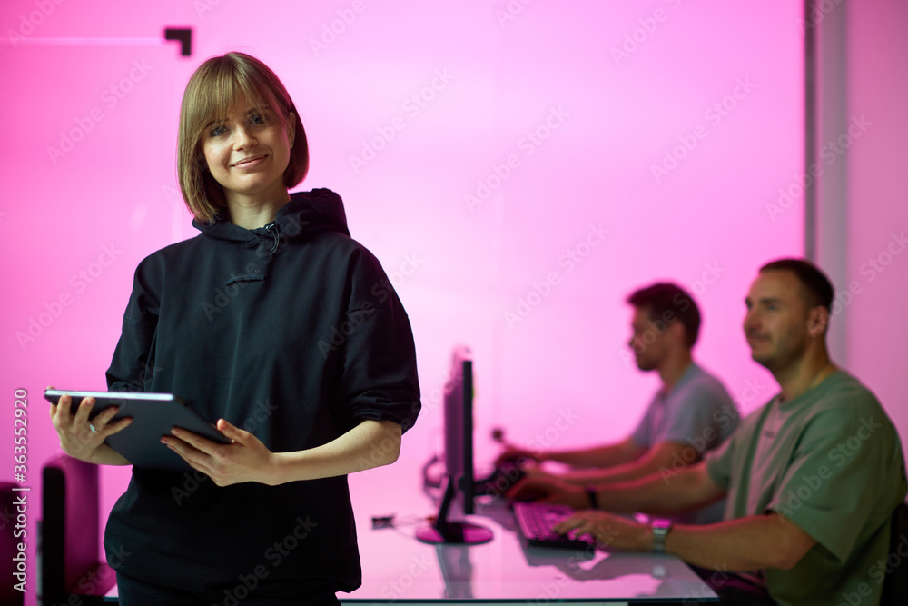 Wall mural Young girl designer stands with tablet at the office during developing a new project, pink background 