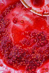 Amaranth surface of squeezed currant. Currant juice, yellow seeds, whole berries in a bowl. Fragment of a cup of smoothie. Vertical image. Copy space. 