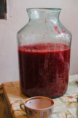 Ten liters glass bottle with squeezed berries for fruit wine. Homemade red wine. The bottle is on the table in a rural kitchen in Ukraine. Vertical image.  Copy space.