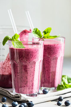 Two glasses of blueberry smoothie with mint garnish on the table.