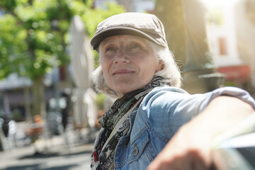 Trendy senior woman with hat relaxing on public bench in small town