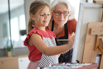 Young girl with grandmother painting on canvas - obrazy, fototapety, plakaty