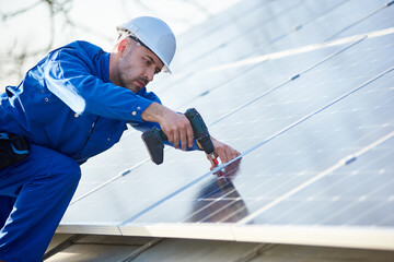 Male engineer in blue suit and protective helmet installing solar photovoltaic panel system using...