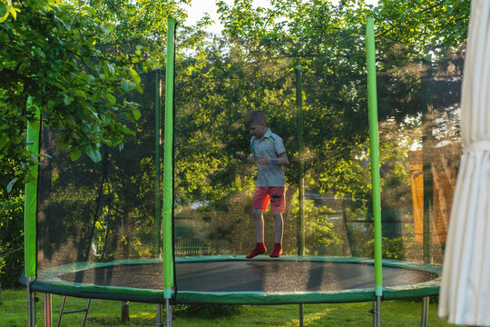 Cheerful eight years old boy having fun on trampoline – jumping with phone in hands.  Action and imagination.
