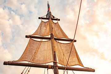 Bottom view of a ship mast with beige sails swings against a blue sky with sunny sunny summer warm...