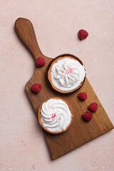 cream cup cakes top view with raspberry on wood cut board at pink background