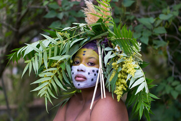 Portrait of proud young African-American woman with face paint and foliage headdress in the...