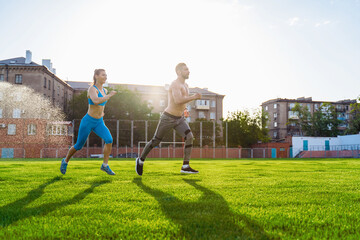 Sportsmen man and woman running in stadium. Healthy sport activity for adults. Young athletes in training, runner exercising. Dynamic run of sprinters in a city stadium on the grass
