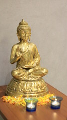 Gold colored Buddha Statue as home decor, surrounded by flowers and lamps