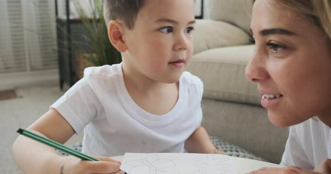Boy whispering a secret to his mother while drawing with colored sketch pen on paper at home