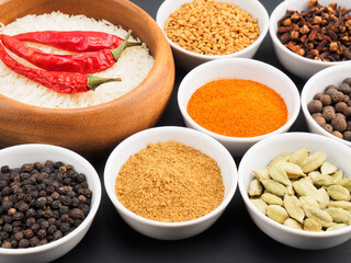 Basmati long, rice, black pepper, masala powder, fenugreek, green cardamom, hot red chili pepper, cloves, tomato on black wooden background. Healthy eating and organic food concept