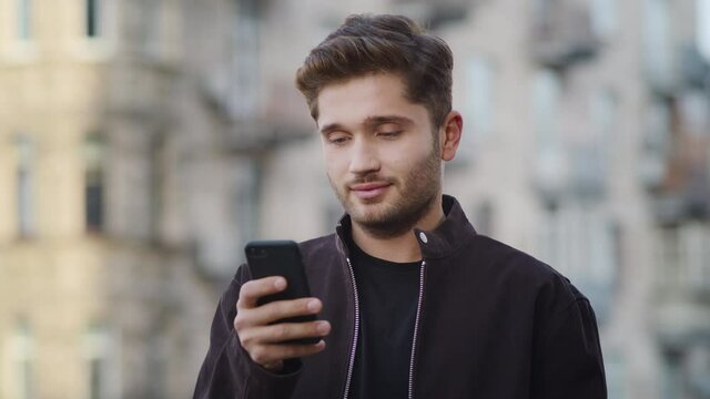Hipster guy receiving message on phone outside. Smiling man looking phone screen
