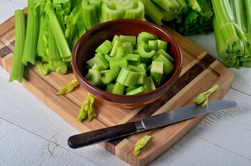 Sliced fresh celery in a clay bowl and Celery stalk on kitchen wooden board
