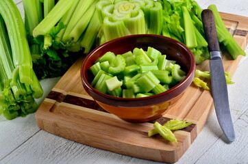 Sliced fresh celery in a clay bowl and Celery stalk on kitchen wooden board