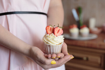 Appetizing cupcake with white cream decorated with fresh strawberries in the hands of a girl.